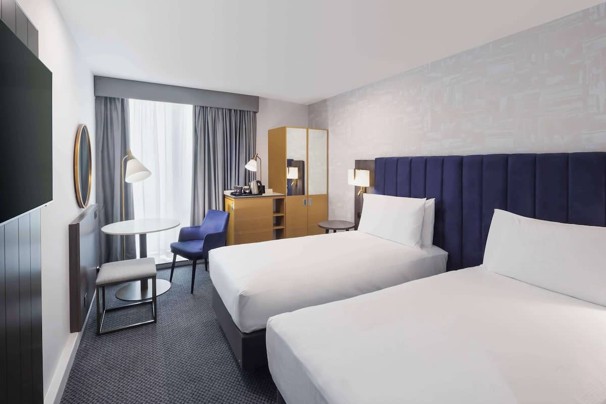 Ein Hotelzimmer mit zwei Betten, einem Schreibtisch, einem Stuhl, einem kleinen Tisch und einem Spiegel.