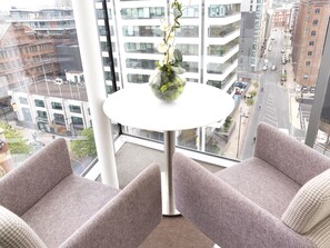 A modern hotel room with a large window, two grey upholstered chairs, and a small white table with a vase of flowers. - DoubleTree by Hilton Manchester - Piccadilly (Manchester)