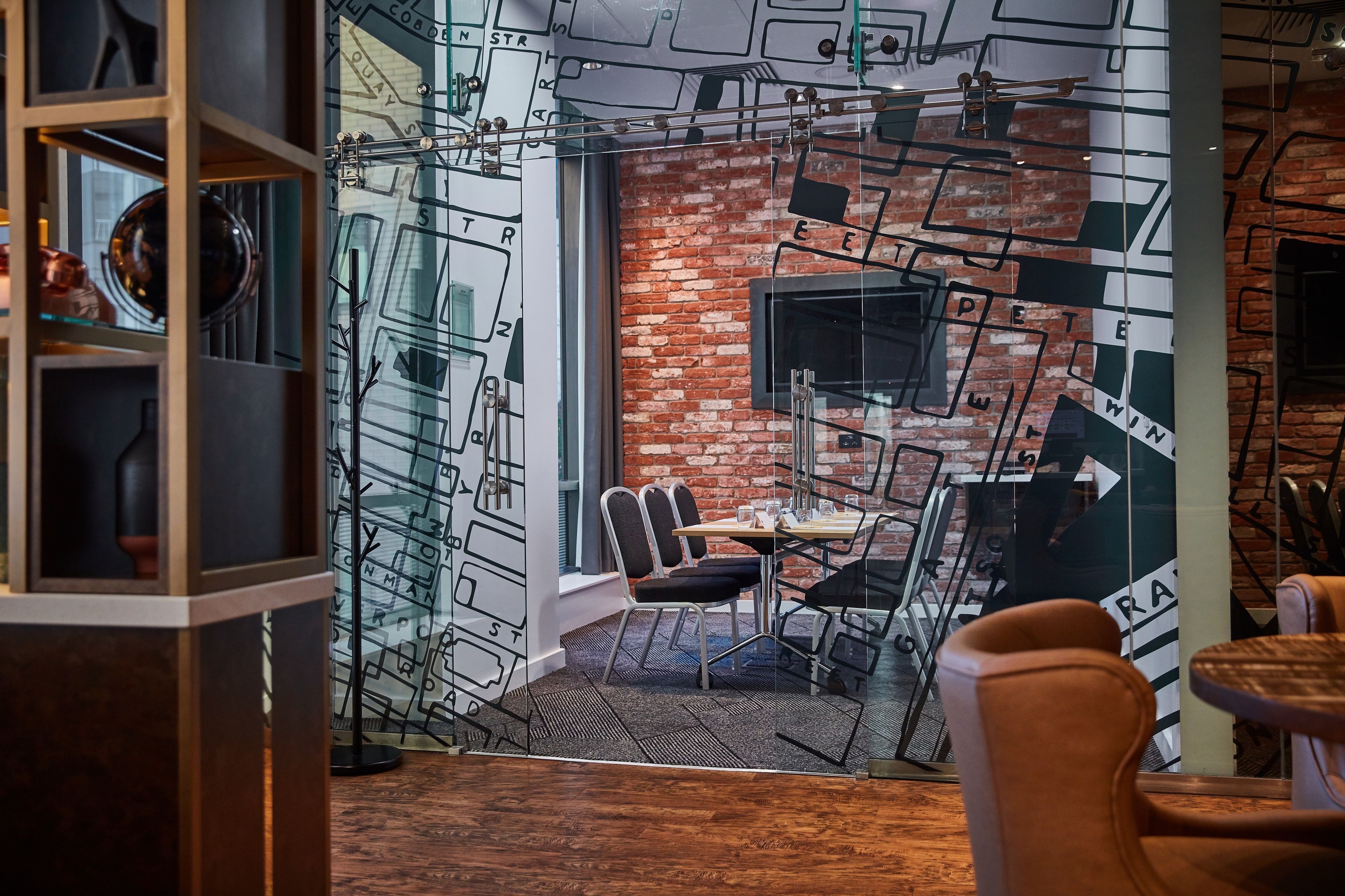 Un interior moderno con pared de ladrillo, separador de vidrio y comedor con sillas y una mesa.
