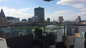 Un balcón con muebles de mimbre, vista al horizonte de la ciudad y un edificio identificado como "CITY TOWER".