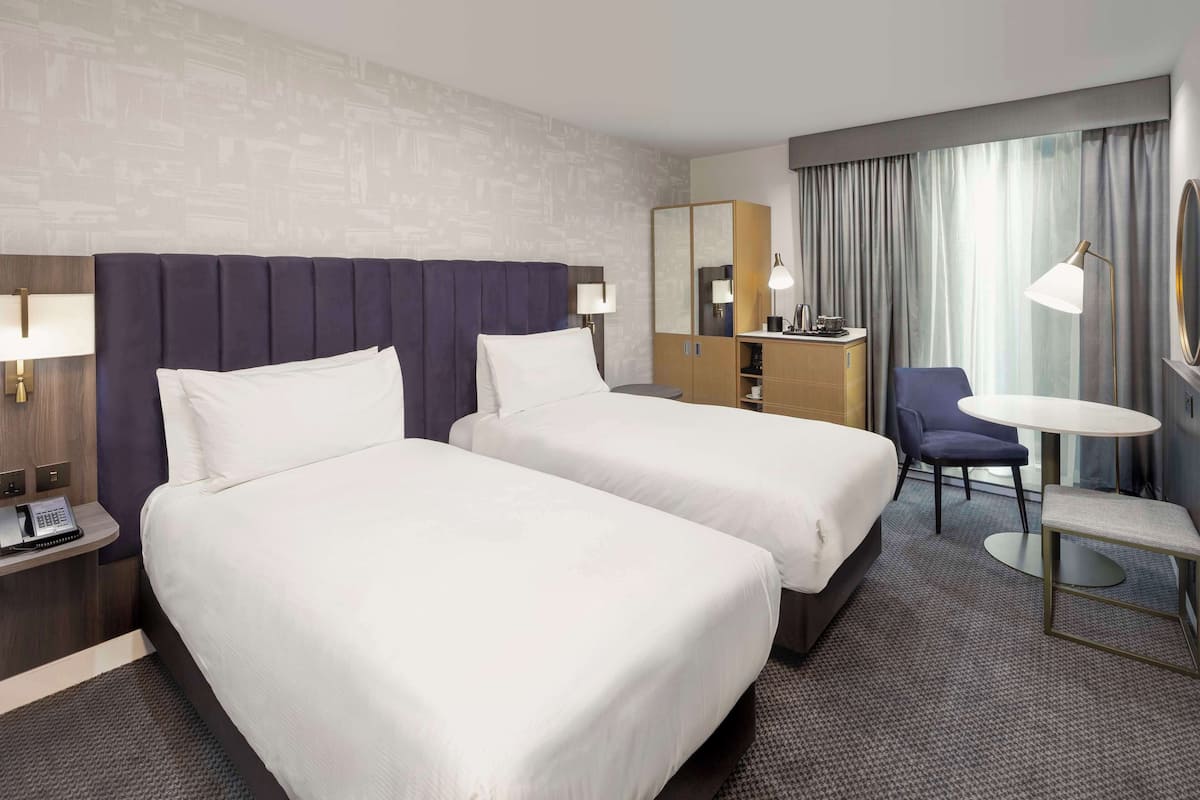 Ein Hotelzimmer mit zwei Betten, einem Schreibtisch, einem Stuhl, einem kleinen Tisch und einem Spiegel.