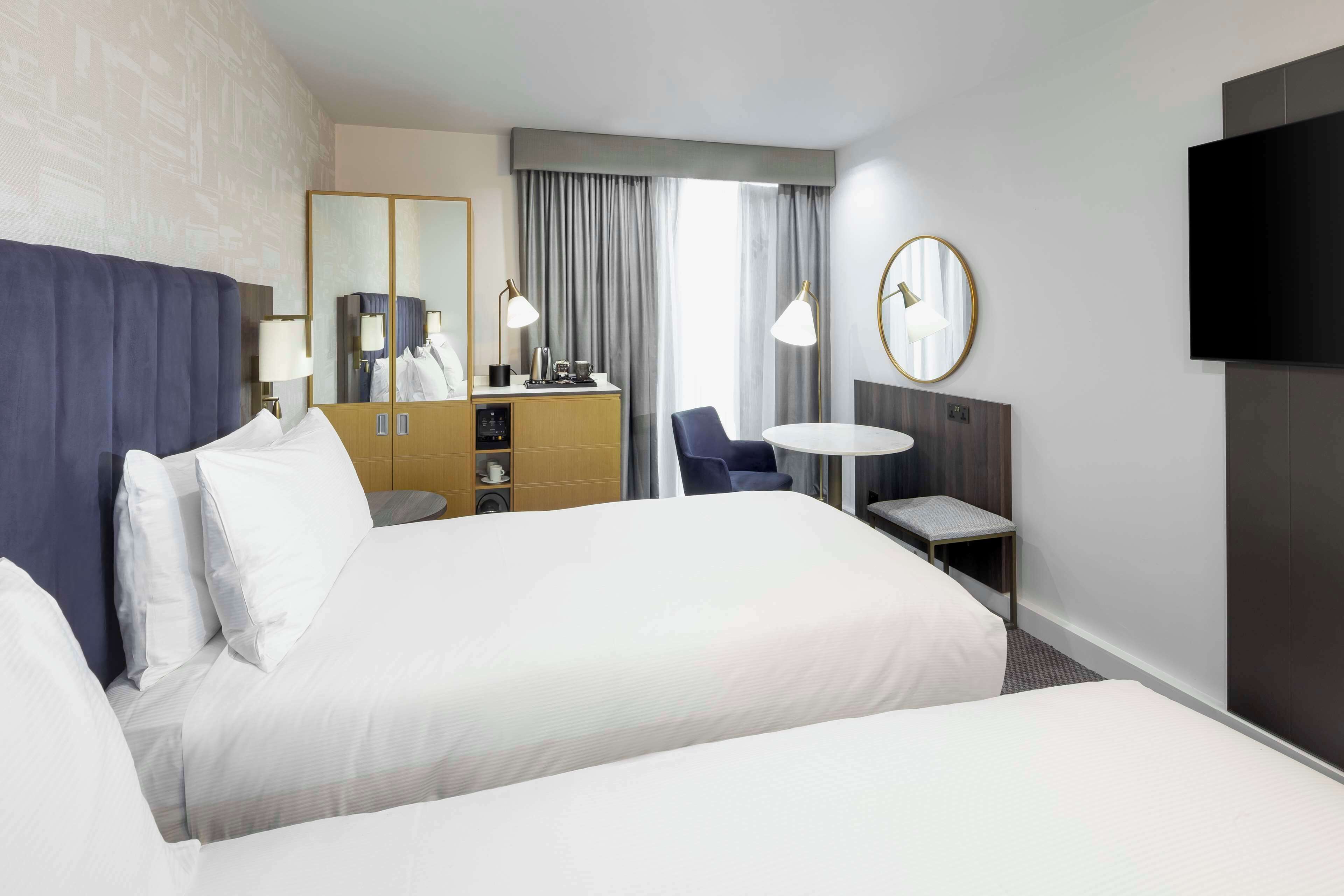 A hotel room with a large bed, a desk, a chair, a TV, and a mirror.