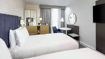 A hotel room with a large bed, a desk, a chair, a TV, and a mirror.