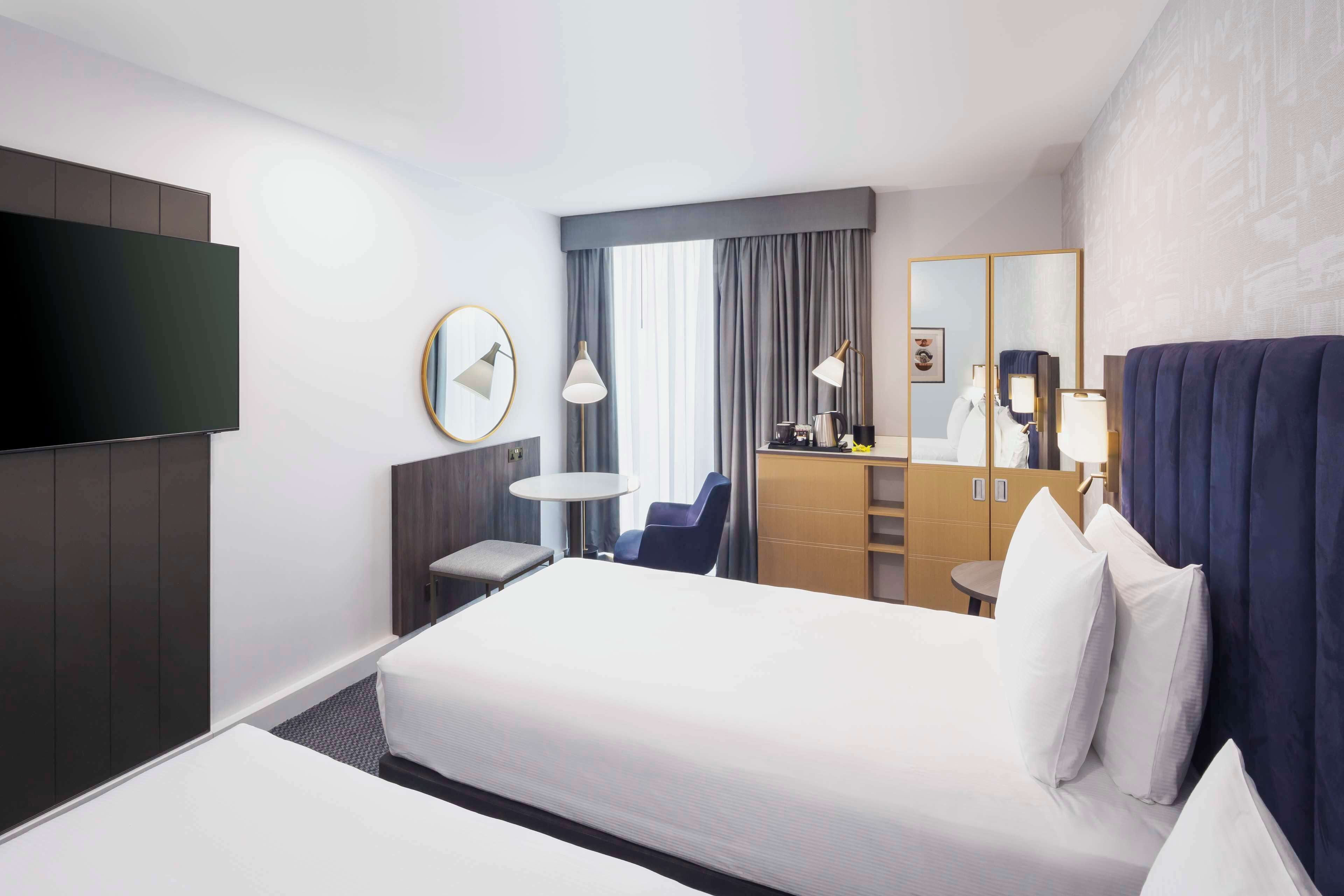 Une chambre d’hôtel avec un grand lit, un bureau, une chaise, une télévision et un miroir.
