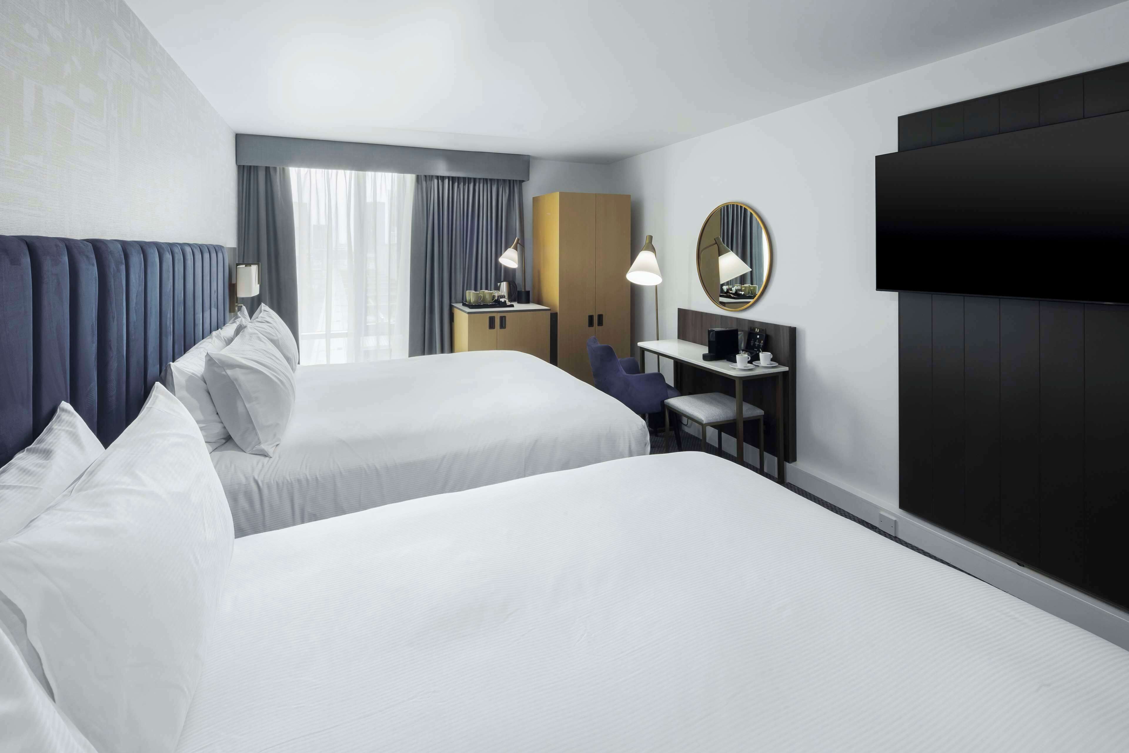 Une chambre d’hôtel avec deux lits, un bureau, une chaise, une télévision et une armoire.