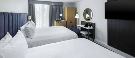 Une chambre d’hôtel avec deux lits, un bureau, une chaise, une télévision et une armoire.