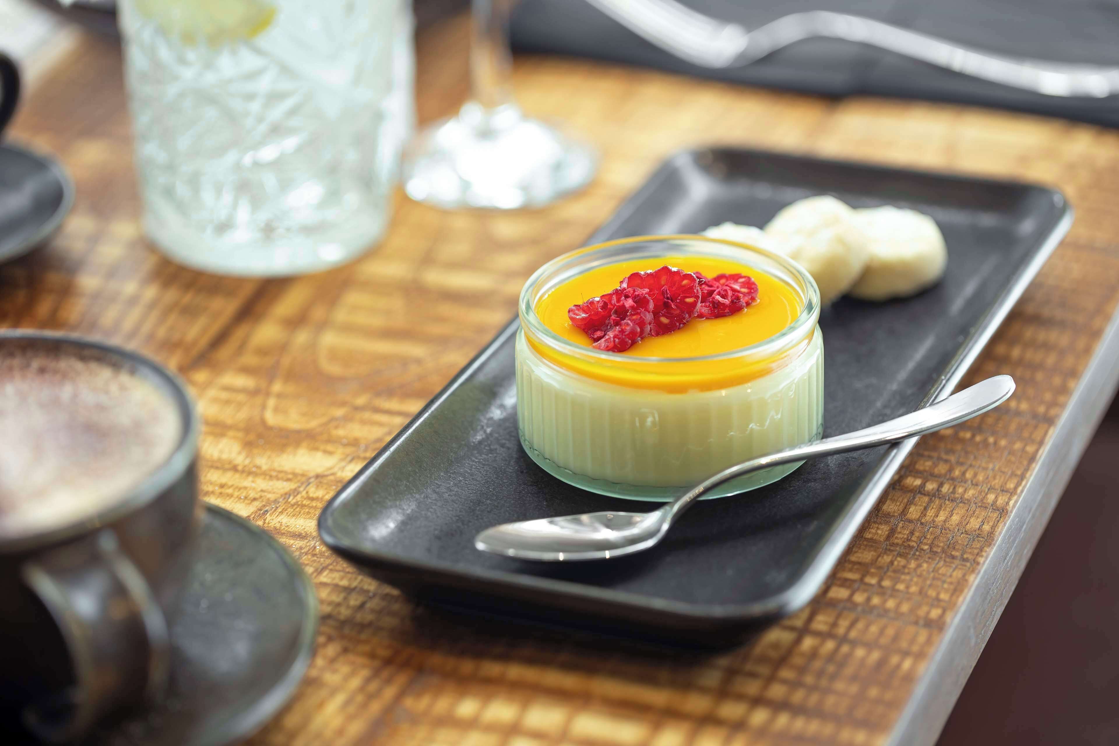 A dessert on a black plate with a spoon, accompanied by a glass of a clear beverage and a cup.