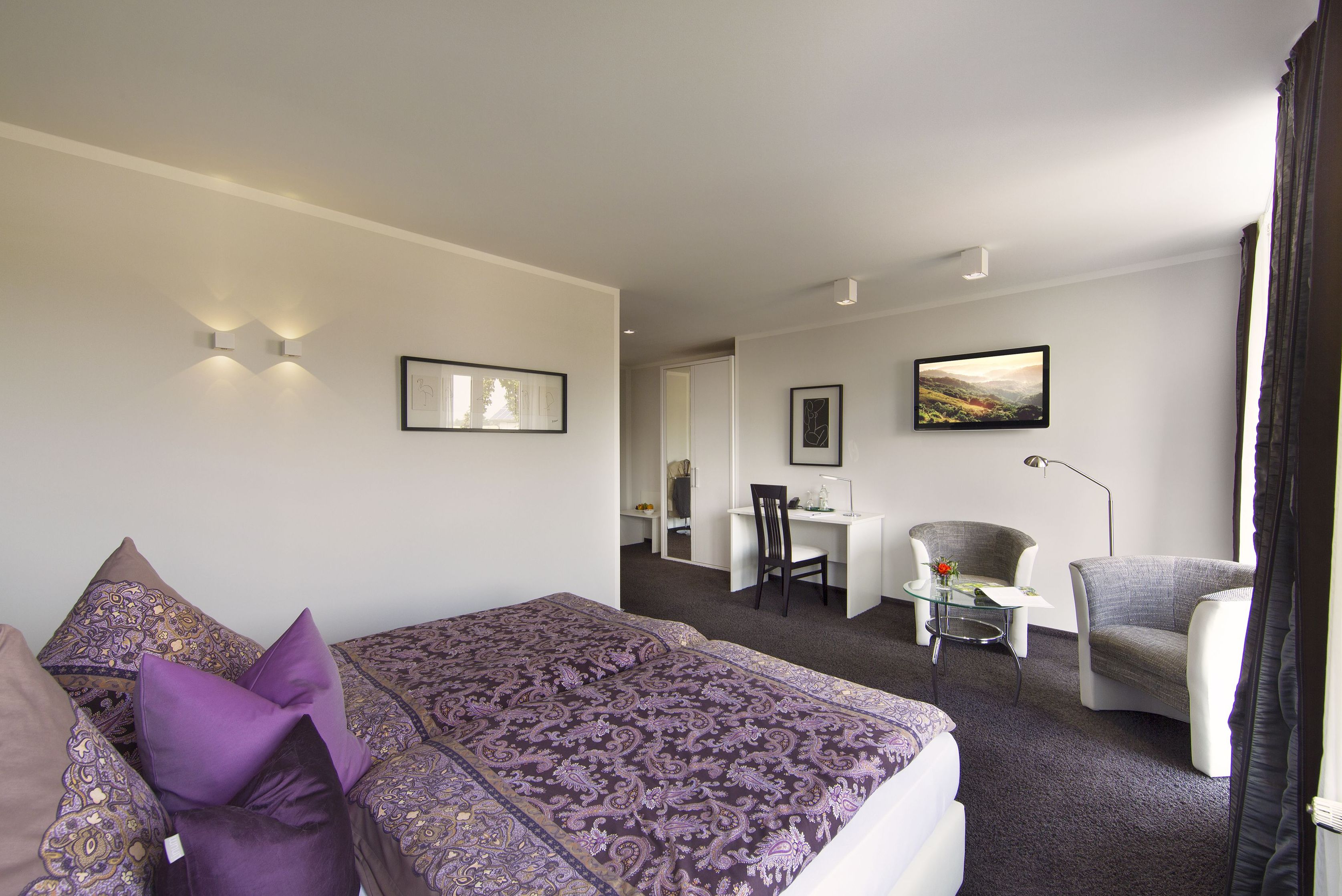 A hotel room with a large bed, a desk, a chair, and a small table.