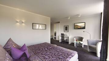 A hotel room with a large bed, a desk, a chair, and a small table.