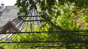 An outdoor dining area with a table set for two, surrounded by chairs, under a metal pergola with greenery. - Landhotel Bartmann (Sendenhorst)