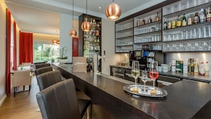 A modern bar area with leather seating, a wine glass tray, and a well-stocked liquor shelf. - Landhotel Bartmann (Sendenhorst)