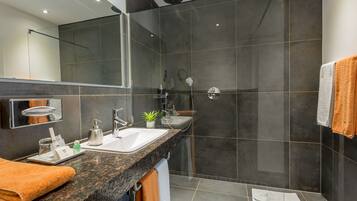 Un baño moderno con encimera de granito, un espejo grande, una ducha y un perchero para toallas.