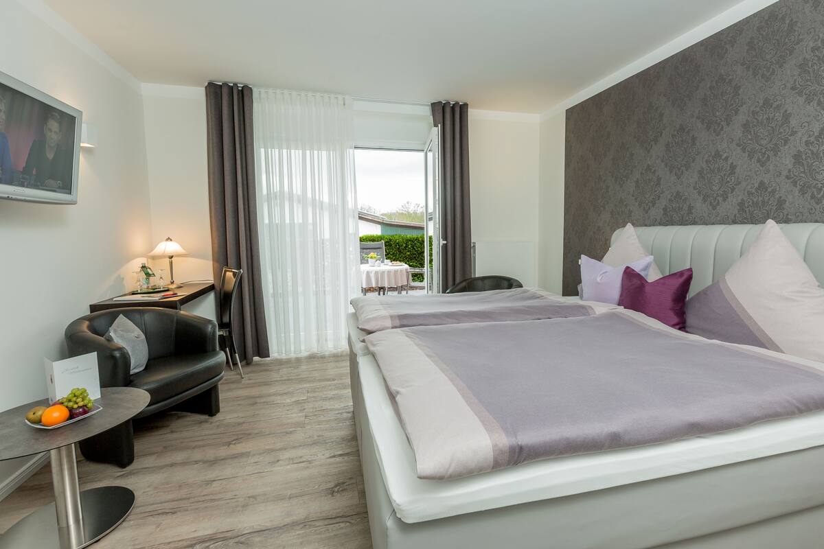 A hotel room with a bed, a desk with a lamp, a chair, and a view of the outdoors.