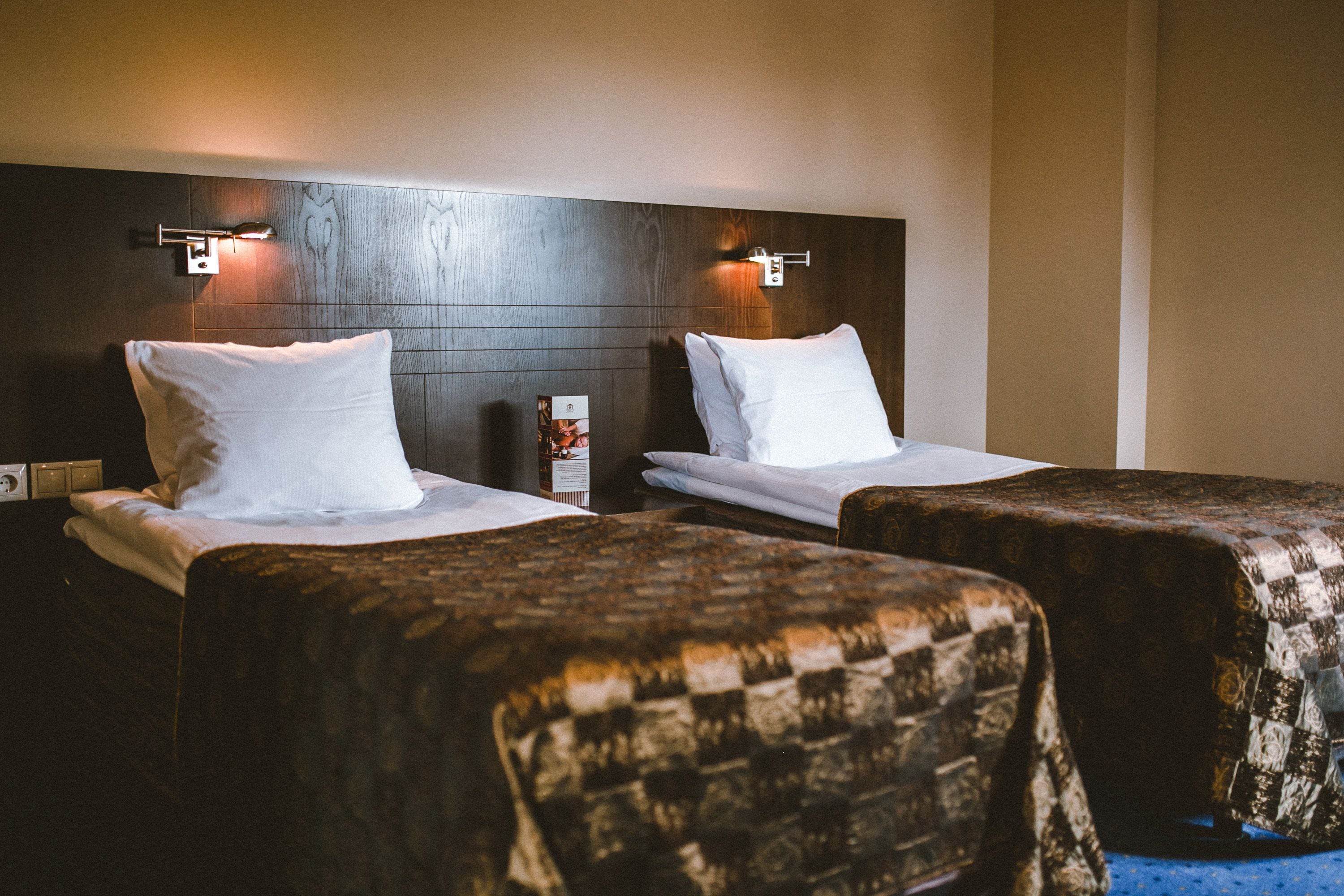 Habitación de hotel con dos camas, cada una con sábanas y almohadas blancas, y cabeceros de madera con luces fijadas a la pared.