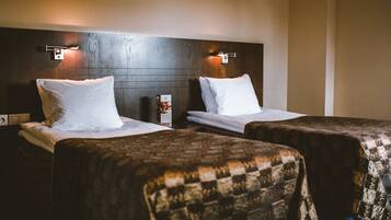 Habitación de hotel con dos camas, cada una con sábanas y almohadas blancas, y cabeceros de madera con luces fijadas a la pared.
