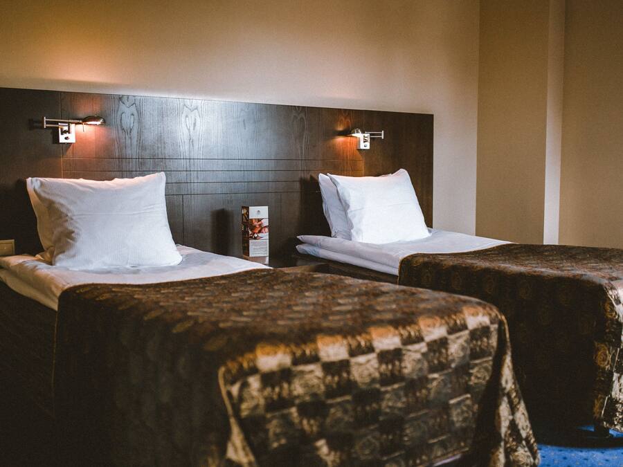 Habitación de hotel con dos camas, cada una con sábanas y almohadas blancas, y cabeceros de madera con luces fijadas a la pared.