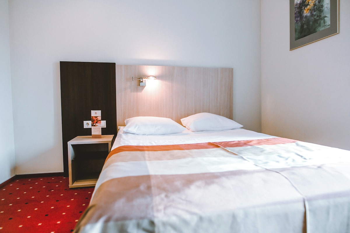 A hotel room with a bed, a nightstand, a wall-mounted light, and a framed picture on the wall.