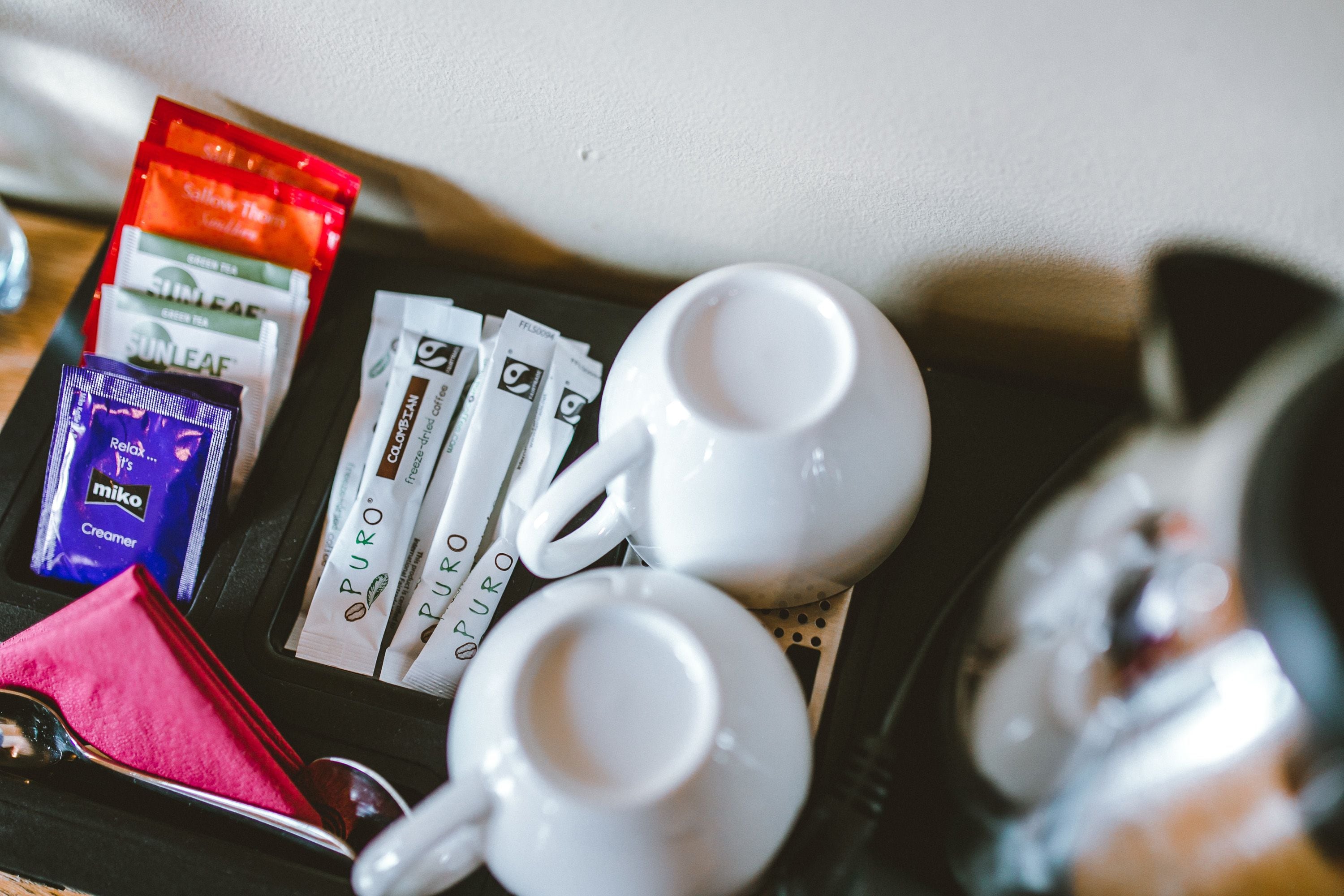 Un plateau avec deux tasses blanches, un paquet rouge et plusieurs dosettes de café.