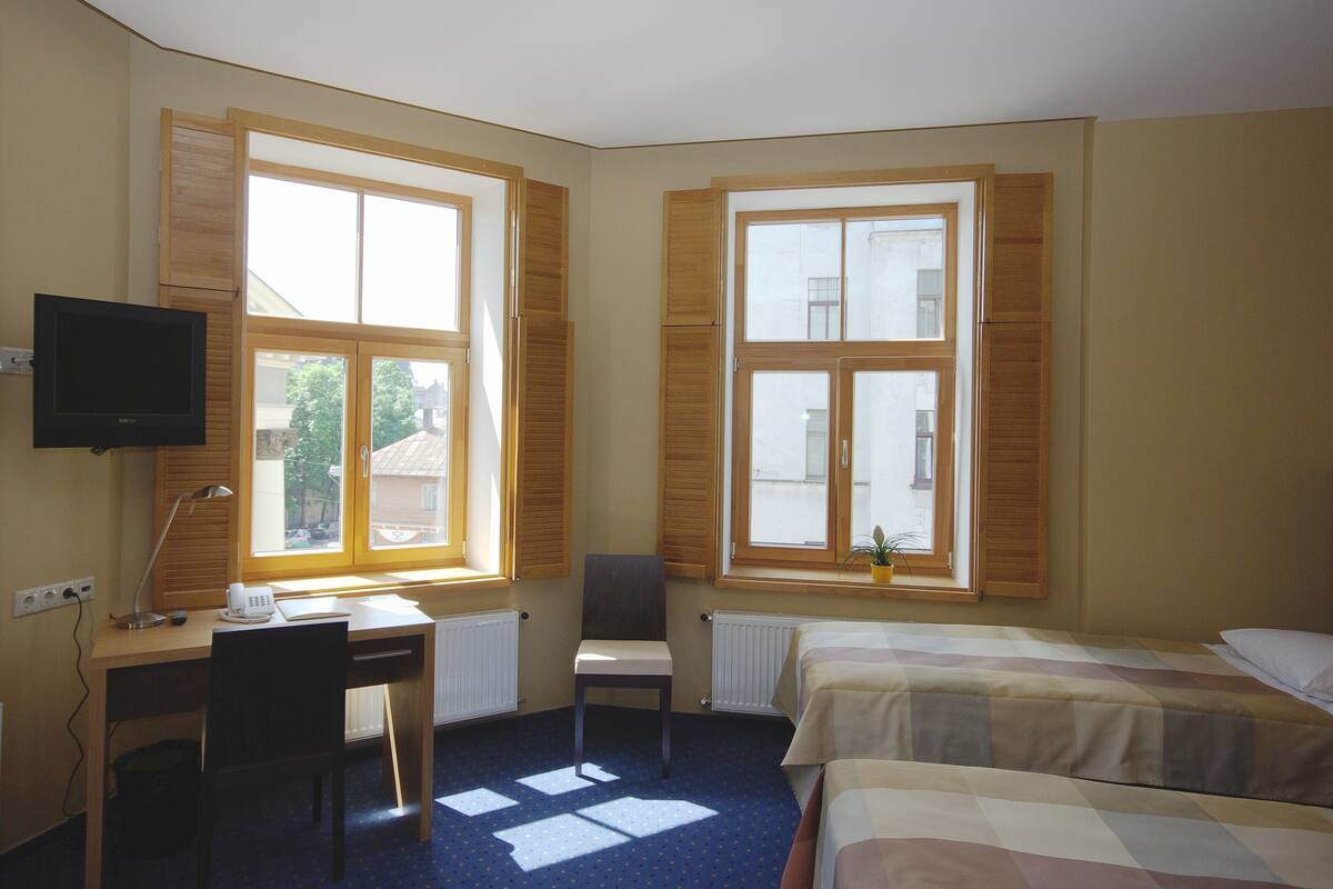Una habitación de hotel con escritorio, silla, televisor, dos camas y ventanas amplias.