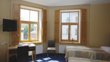 Hotellihuone, jossa on työpöytä, tuoli, televisio, kaksi sänkyä ja suuret ikkunat.