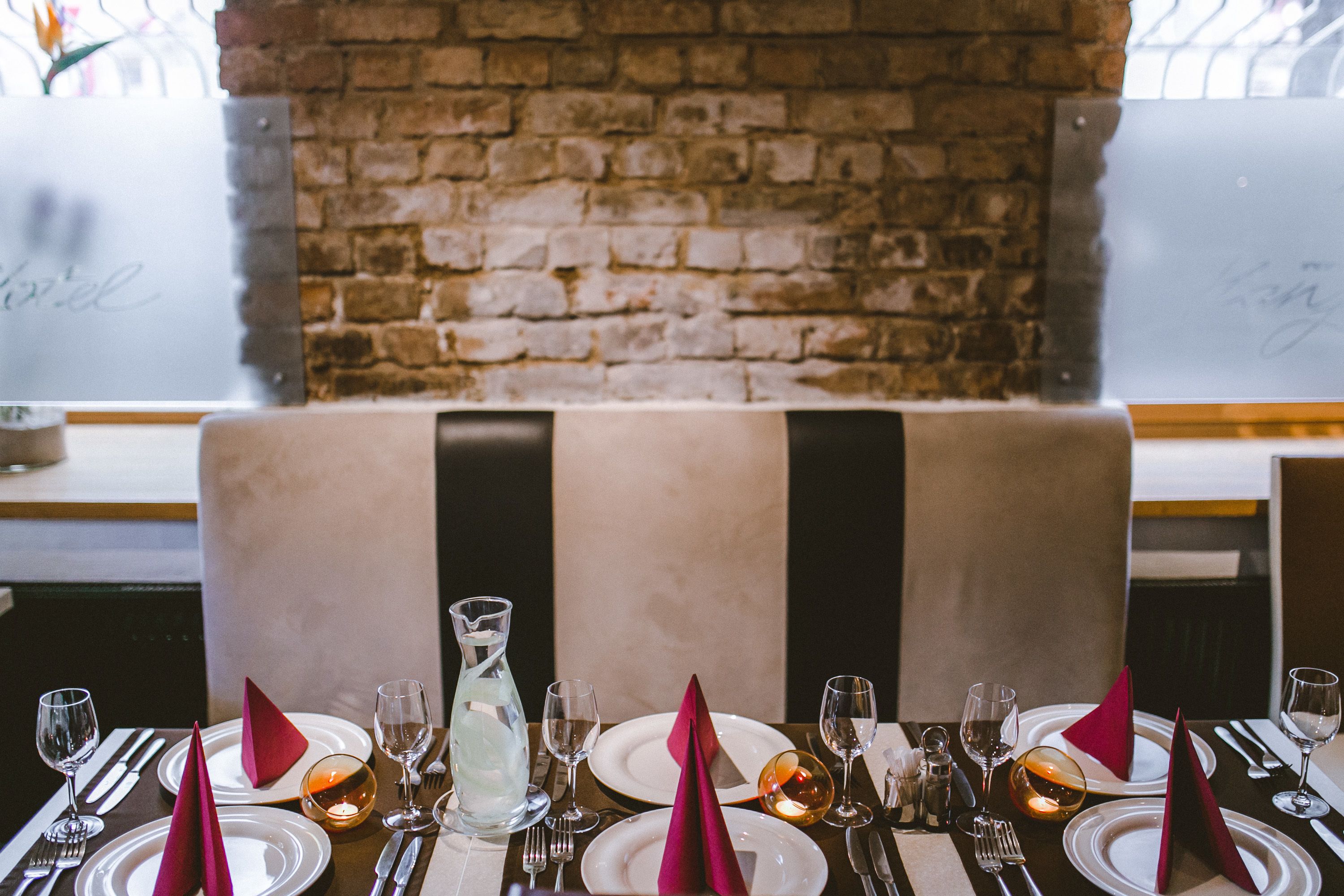 A restaurant setting with a brick wall, a booth, and a table set for a meal.