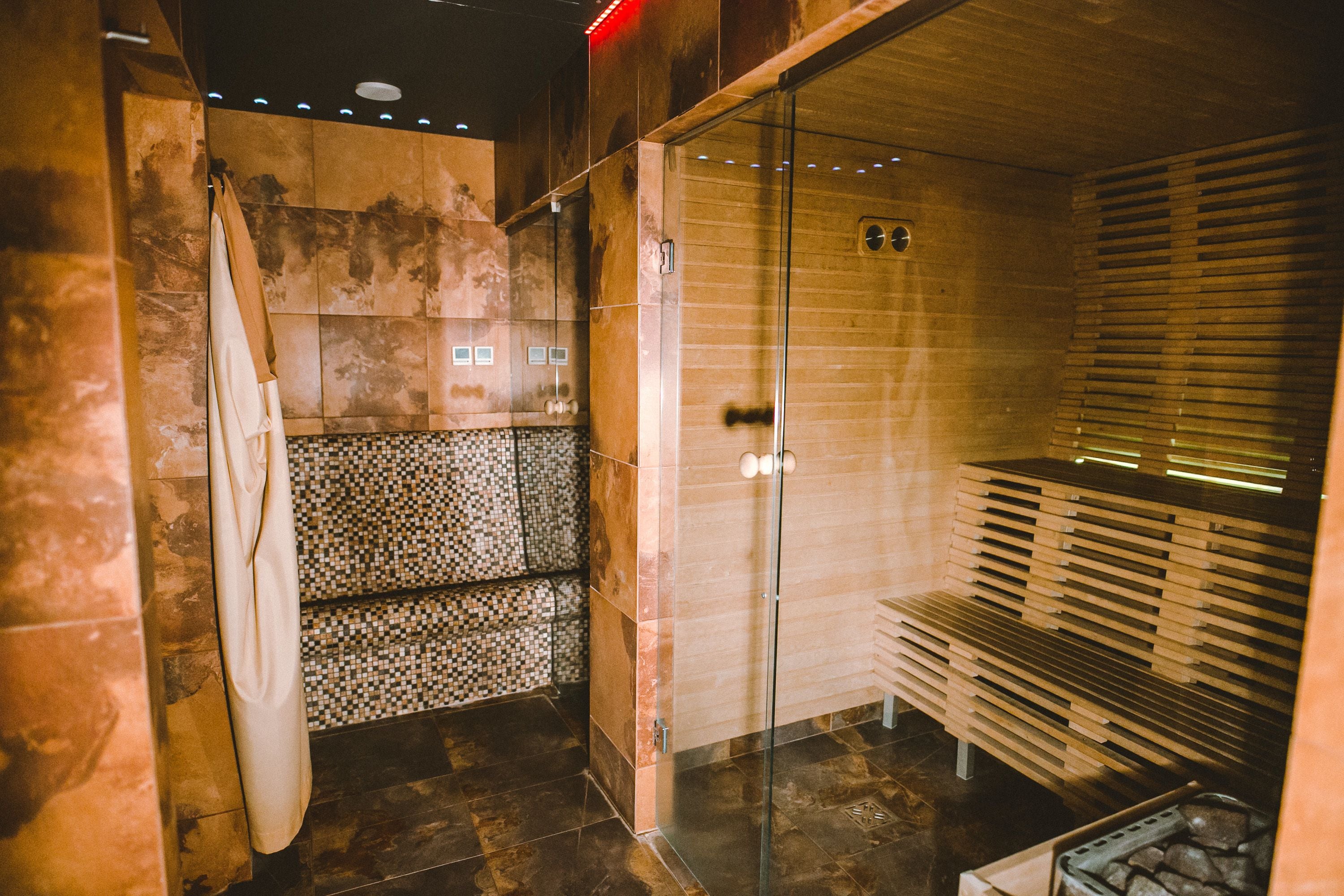 Una sauna con puerta de vidrio, bancos de madera y pared de baldosas.