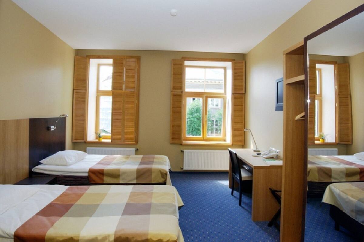 Habitación de hotel con dos camas, un escritorio y una ventana con persianas.