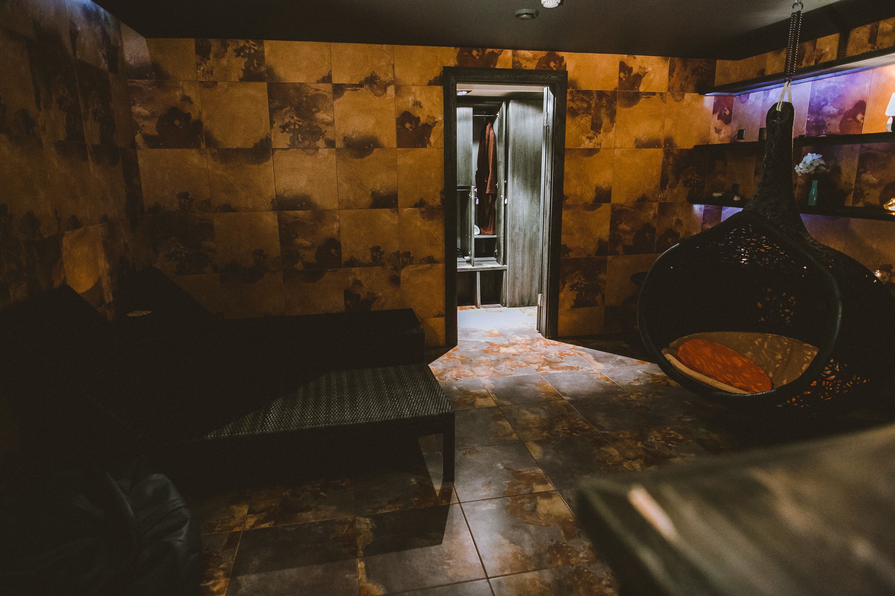 A room with a stone wall, a bench, a hanging chair, and a door leading to another room.