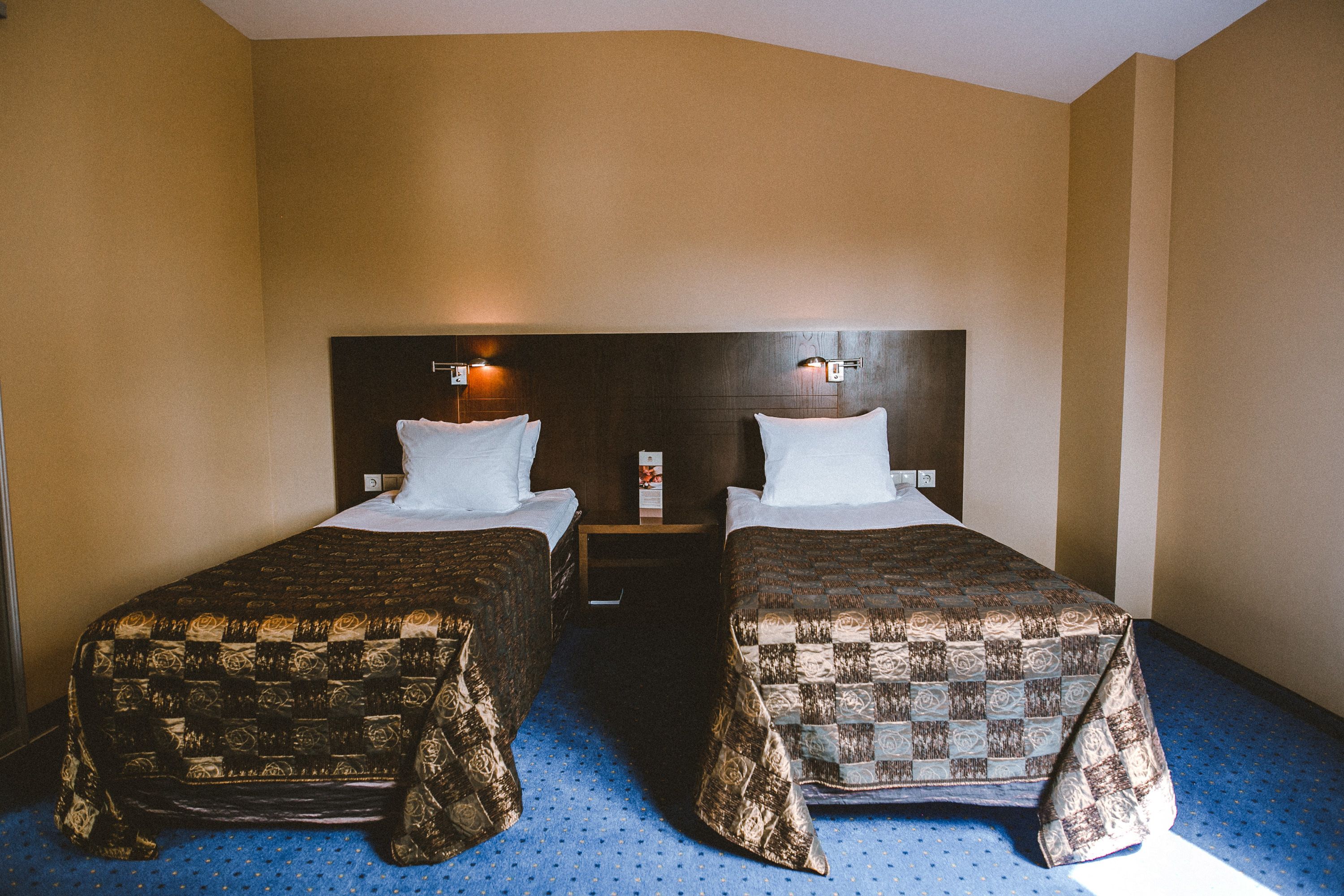Habitación de hotel con dos camas, cabecera de madera y alfombra azul.