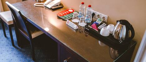 A hotel room desk with a telephone, a notepad, a pen, a glass of water, a bottle of water, a coffee pot, and a small box of tissues.