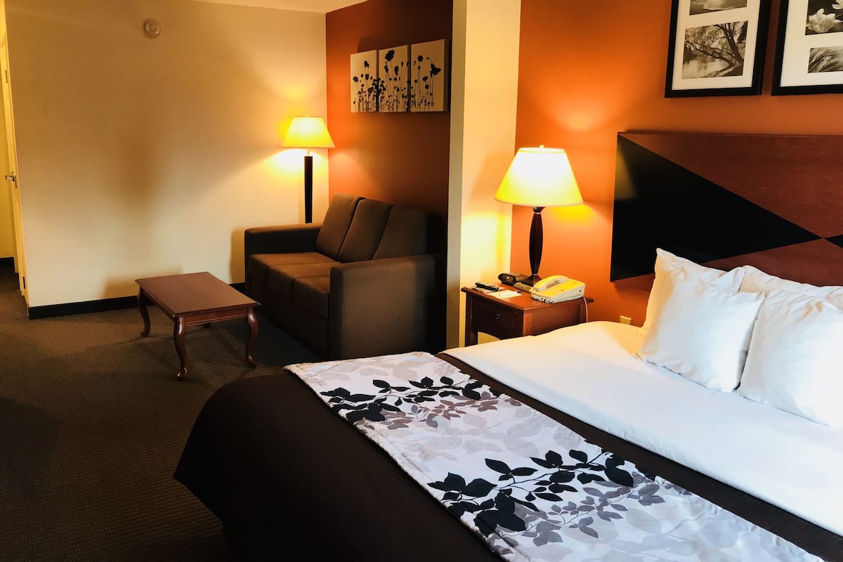 Habitación de hotel con cama, dos sillas, una mesita, una lámpara, un teléfono y una pared decorada con cuadros.