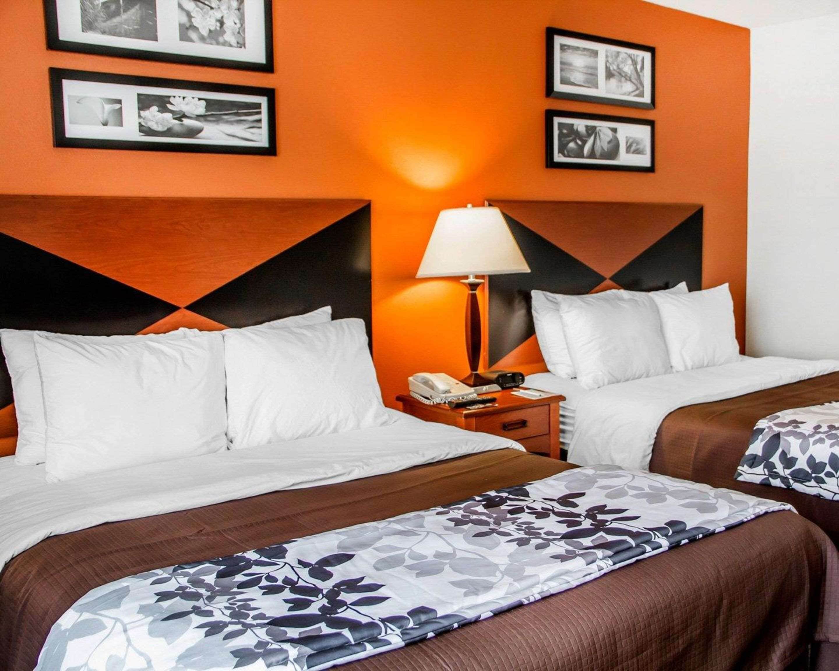 A hotel room with two beds, a nightstand with a lamp, and framed pictures on the wall.