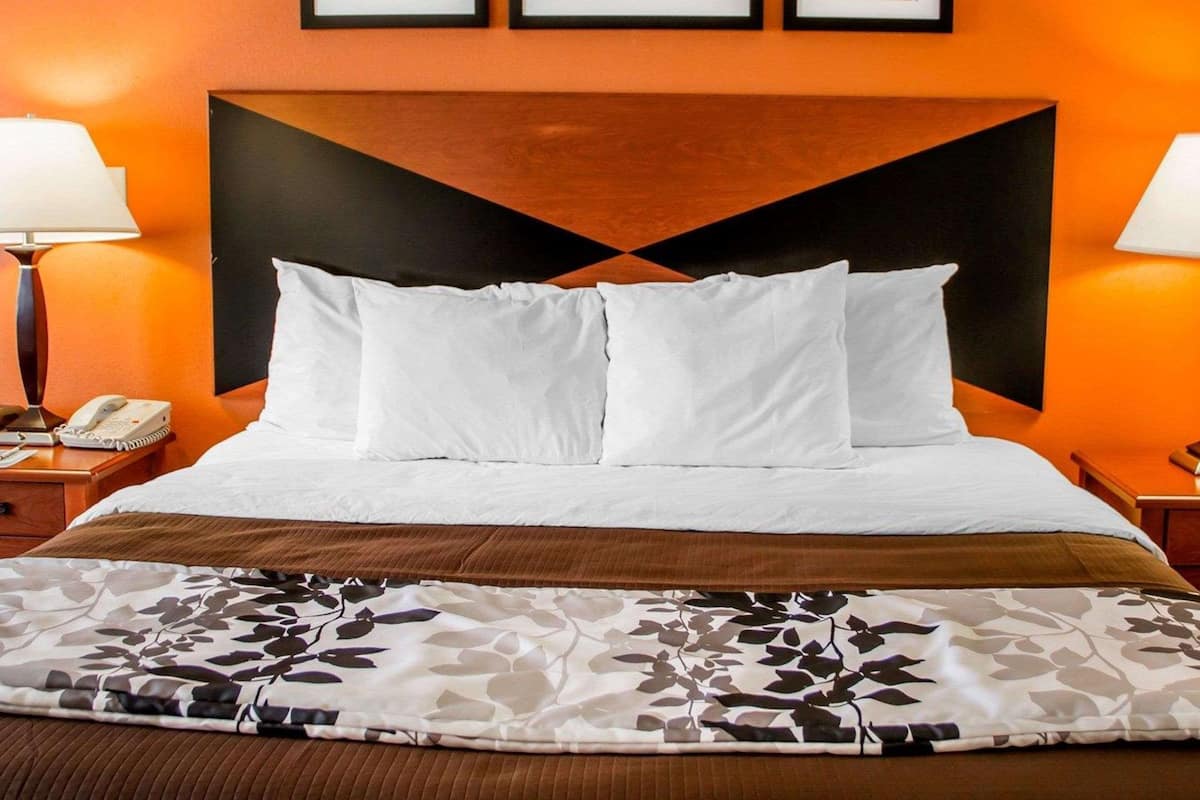 Habitación de hotel con una cama grande, ropa de cama blanca, un plaid estampado de flores y una pared con cuadros enmarcados.