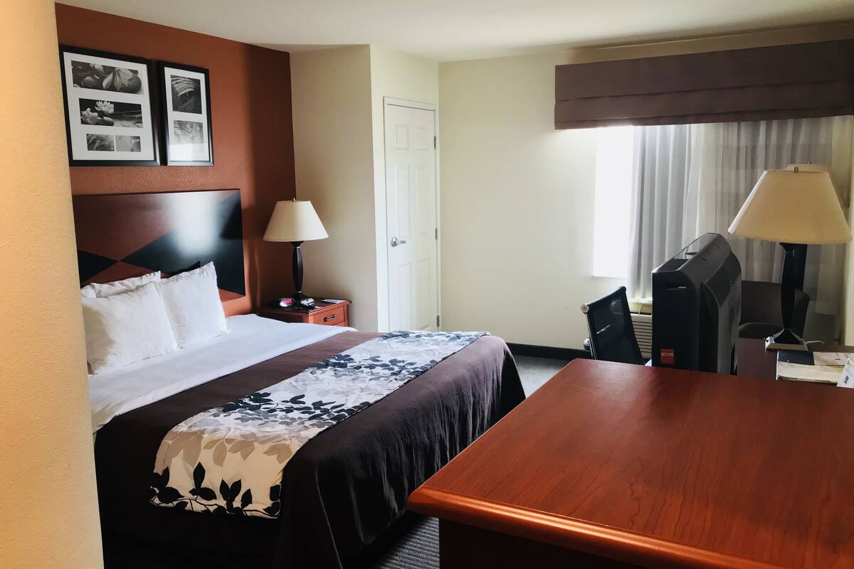 Una habitación de hotel con cama, mesita de noche, lámpara, escritorio y silla.