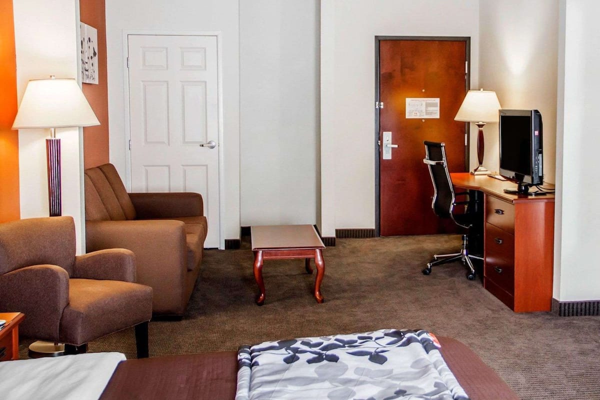 Una habitación de hotel con cama, escritorio con computadora, silla y sofá.