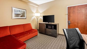 Una habitación de hotel con sofá rojo, televisión, microondas, escritorio y puerta.
