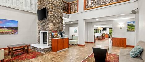 A spacious lobby with a stone fireplace, wooden flooring, and a high ceiling.