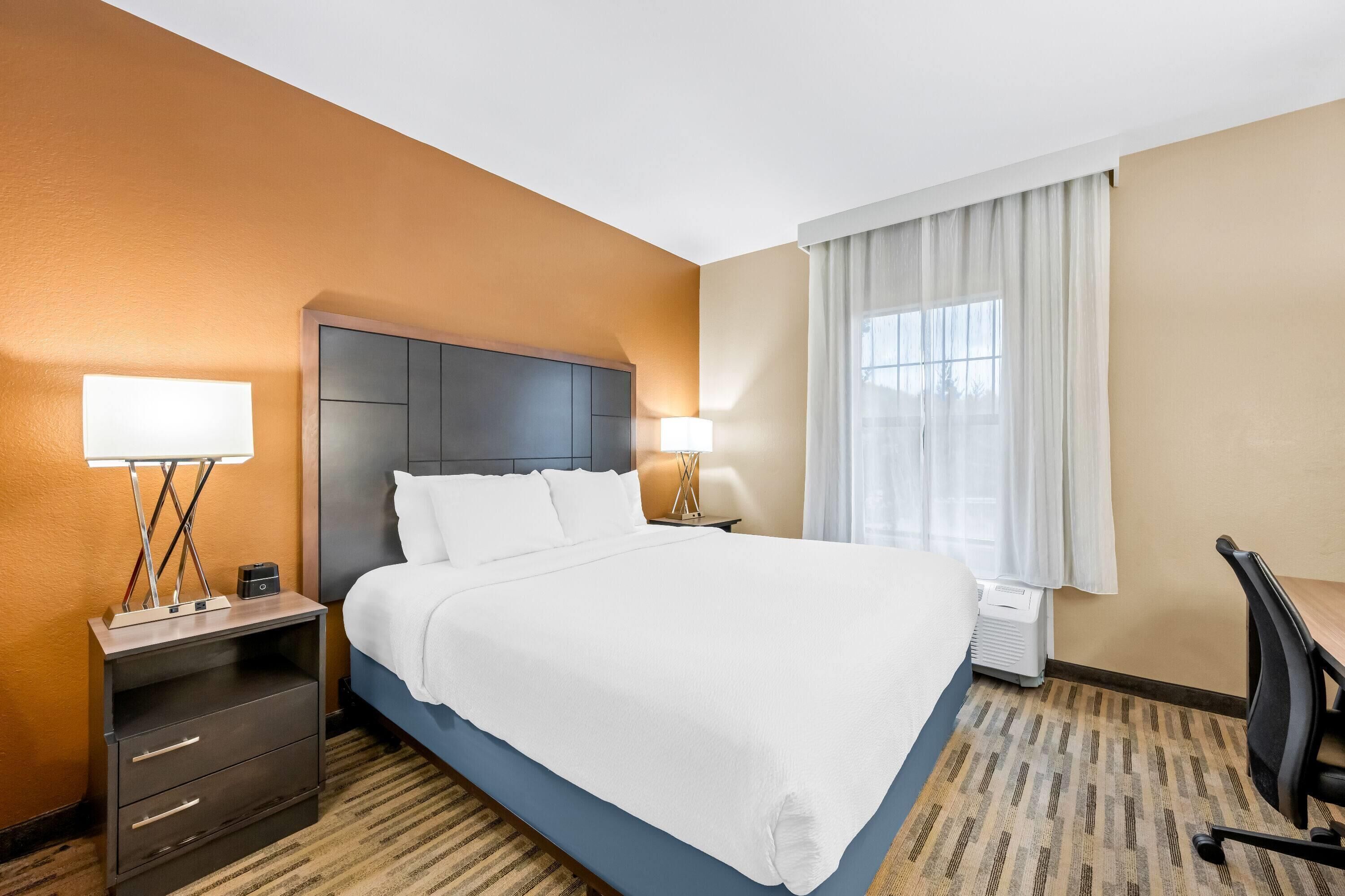 Una habitación de hotel con una cama grande, dos mesitas de noche con lámparas, un escritorio y una silla.