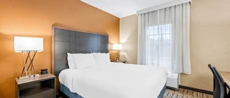 Una habitación de hotel con una cama grande, dos mesitas de noche con lámparas, un escritorio y una silla.