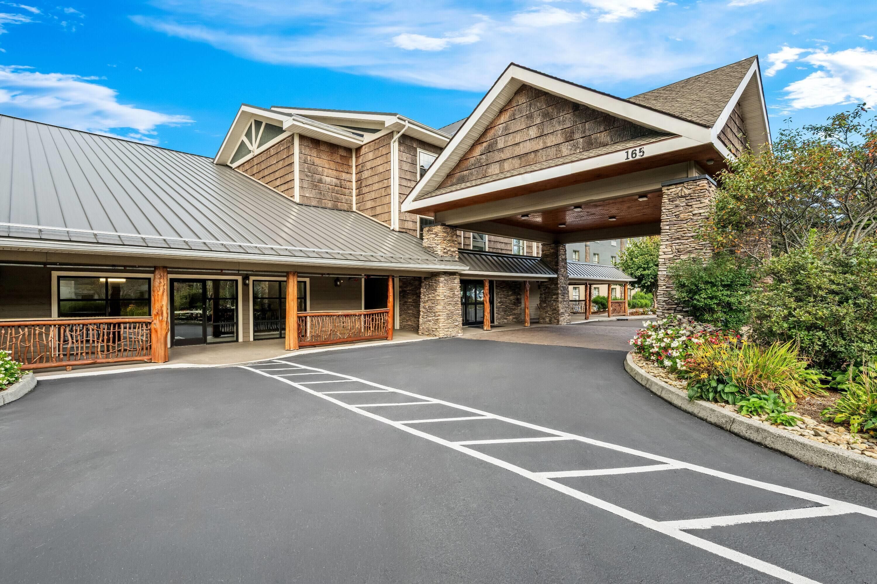 A modern building with a covered entrance, stone facade, and a parking area with marked spaces.