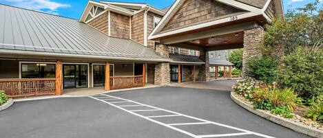 A modern building with a covered entrance, stone facade, and a parking area with marked spaces.