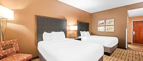 A hotel room with two beds, a chair, a lamp, and framed pictures on the wall.