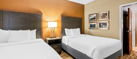 A hotel room with two beds, a nightstand, a lamp, and a door.