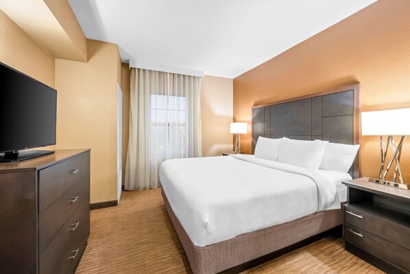 Une chambre d’hôtel avec un grand lit, un téléviseur posé sur une commode, une lampe et une fenêtre avec des rideaux.