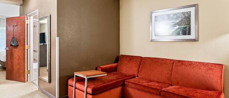 Una habitación de hotel moderna con un sofá de terciopelo rojo, una mesita de madera pequeña y un cuadro en la pared.