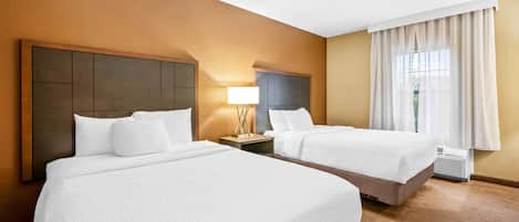 A hotel room with two beds, a nightstand with a lamp, and a window with curtains.
