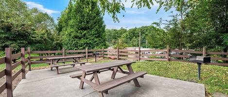 A picnic area with benches and a wooden fence, surrounded by trees and greenery.