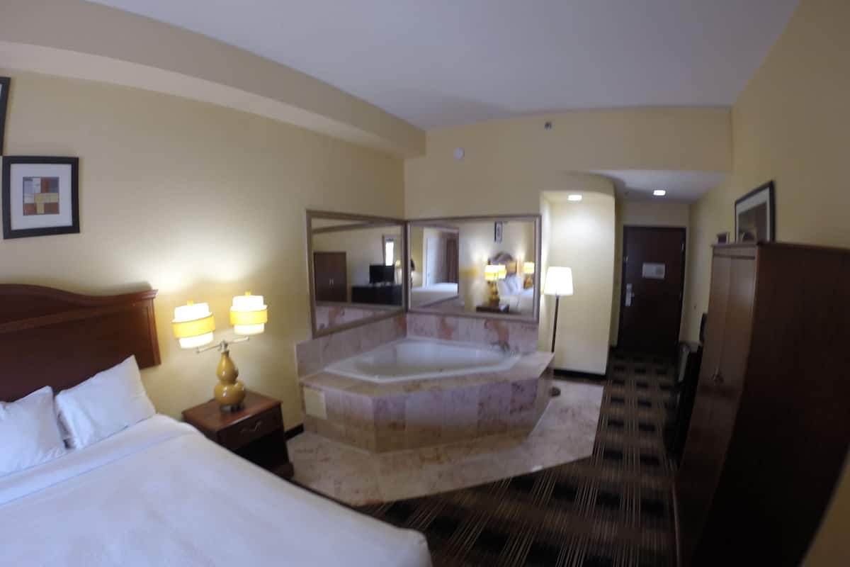 Hotelkamer met een groot bed, een zithoek met een stoel en een tafel, een ruim bad en een spiegel.