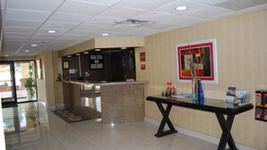 A reception area with a reception desk, a glass-top table with magazines, and a framed artwork on the wall. - Jameson Inn and Suites Riverdale (Riverdale)