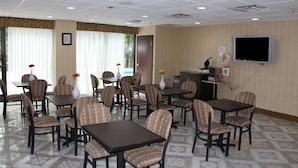 A hotel room with a dining area featuring multiple tables and chairs, a television mounted on the wall, and a window with curtains. - Jameson Inn and Suites Riverdale (Riverdale)